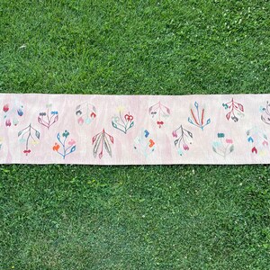 May include: A pink runner rug with a floral pattern. The rug has a fringe border and features a repeating design of stylized flowers in shades of pink, blue, green, and red.