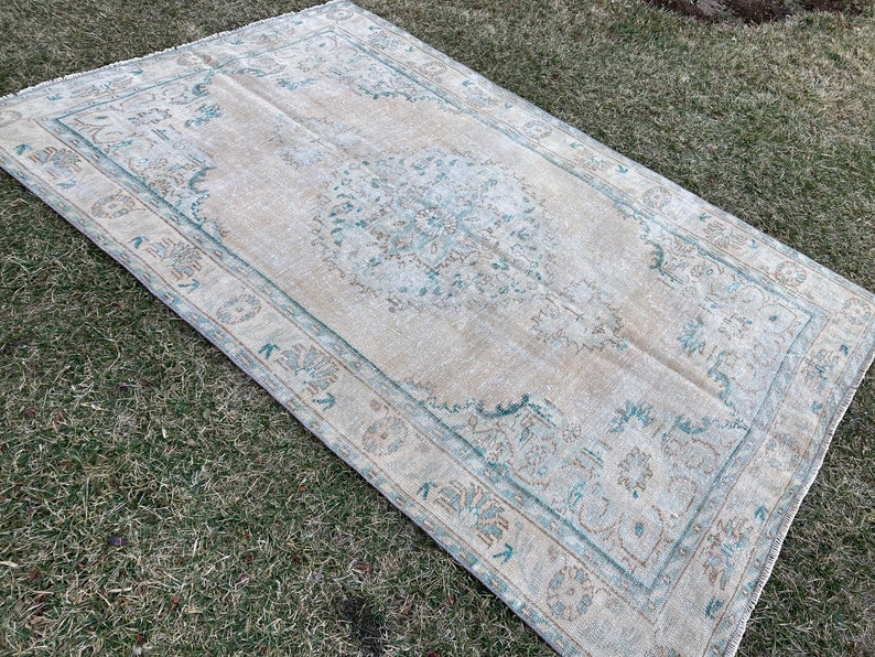May include: A vintage rug with a light beige background and a teal blue floral pattern. The rug has a distressed look and is perfect for adding a touch of bohemian style to any room.