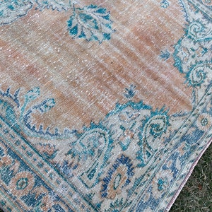 May include: A vintage rug with a faded peach background and a blue and white floral pattern. The rug has a distressed look and is perfect for adding a touch of bohemian style to any room.