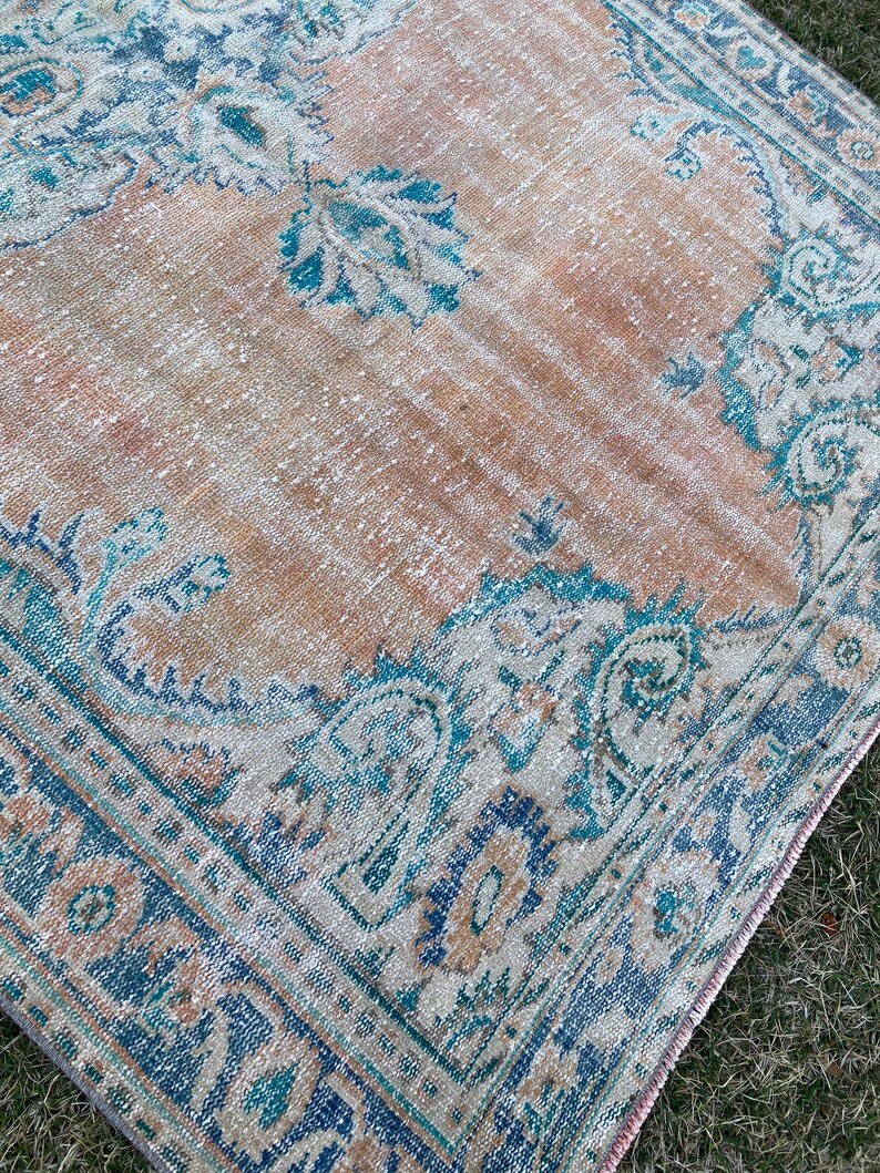 May include: A vintage rug with a faded peach background and a blue and white floral pattern. The rug has a distressed look and is perfect for adding a touch of bohemian style to any room.