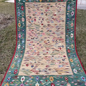 May include: A traditional Turkish rug with a green and beige colour scheme. The rug features a floral pattern with intricate details. The rug has a fringed border.