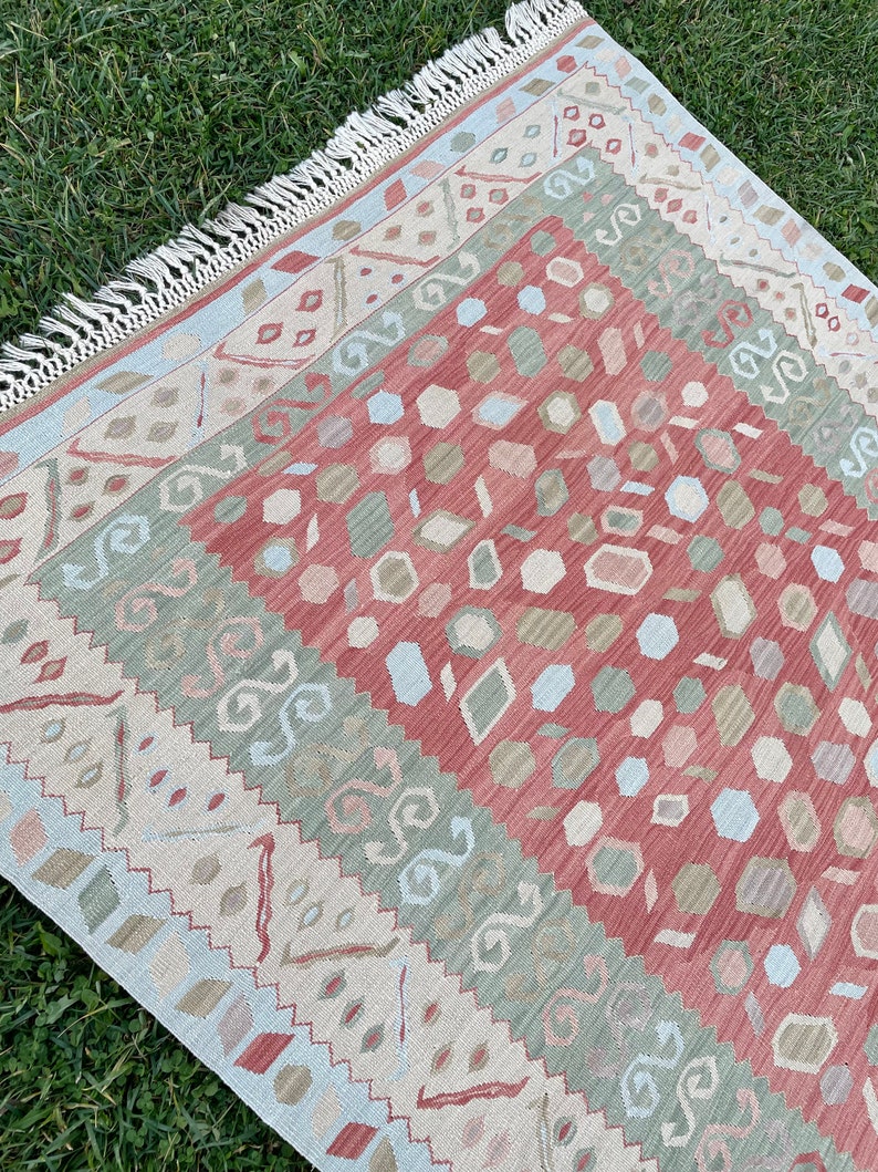 K&ouml;nnte beinhalten: Ein mehrfarbiger Teppich mit geometrischem Muster. Der Teppich hat einen Fransenrand und ist aus weichem, gewebtem Material.