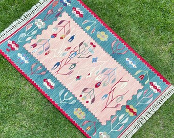 Puede incluir: Una alfombra rosa y azul con un patrón floral. La alfombra tiene un borde de flecos y está hecha de lana.