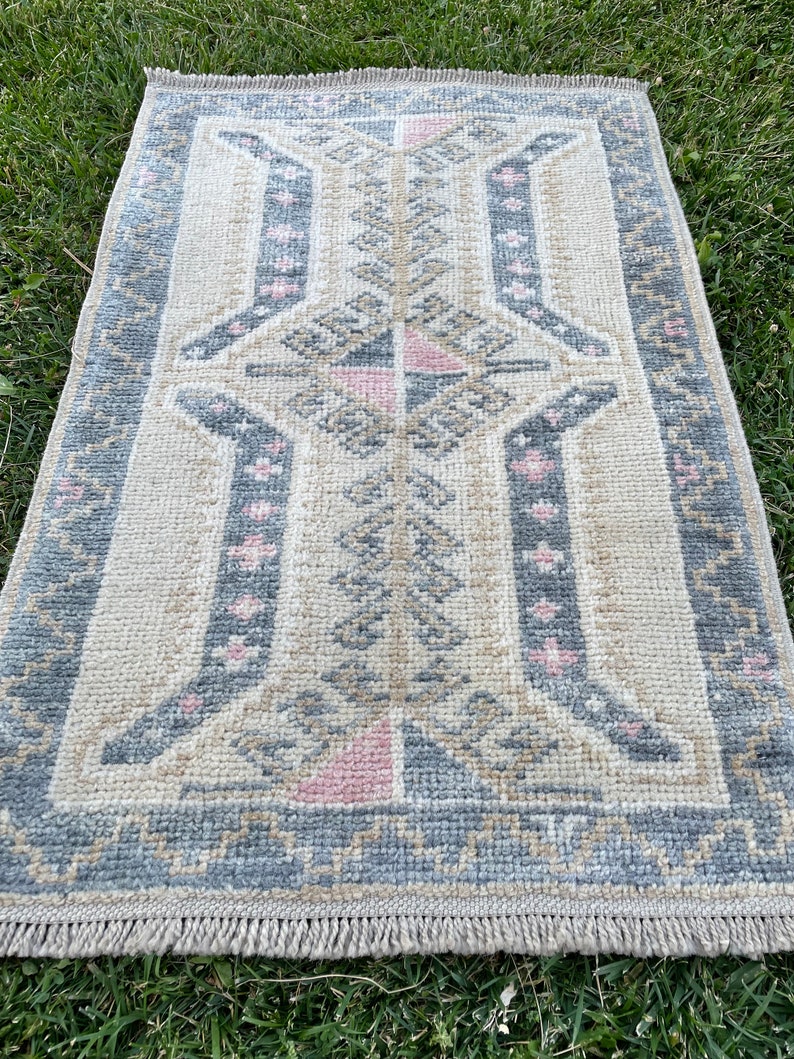Puede incluir: Una alfombra beige y gris con patrones y acentos rosados. La alfombra tiene un borde de flecos y un dise&ntilde;o geom&eacute;trico.