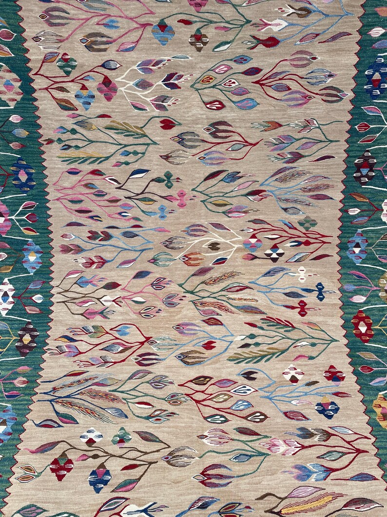 May include: A beige rug with a colourful floral pattern. The rug has a green border with geometric designs.