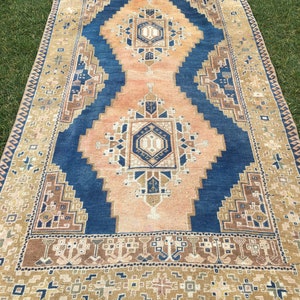 May include: A vintage rug with a blue and peach colour scheme. The rug has a geometric pattern with a central medallion. The rug has a fringe border.