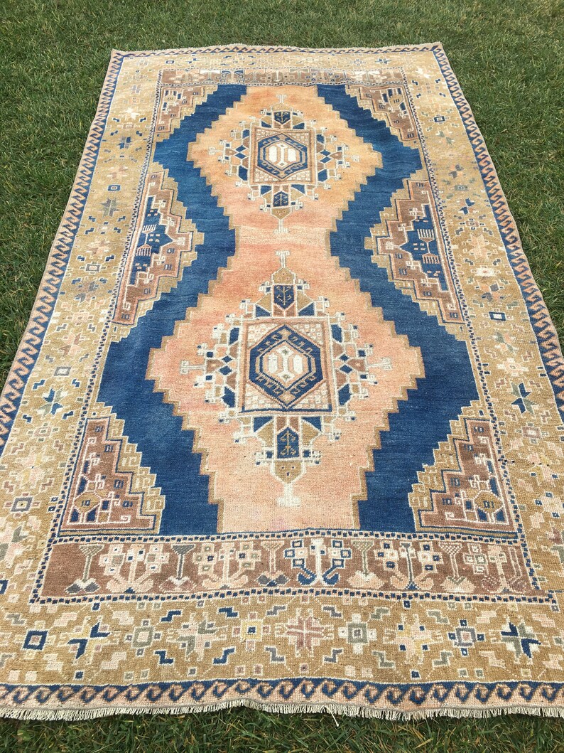 May include: A vintage rug with a blue and peach colour scheme. The rug has a geometric pattern with a central medallion. The rug has a fringe border.