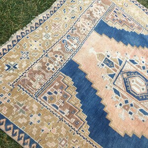 May include: A vintage rug with a blue, beige and brown geometric pattern. The rug has a fringed edge and is made of wool.