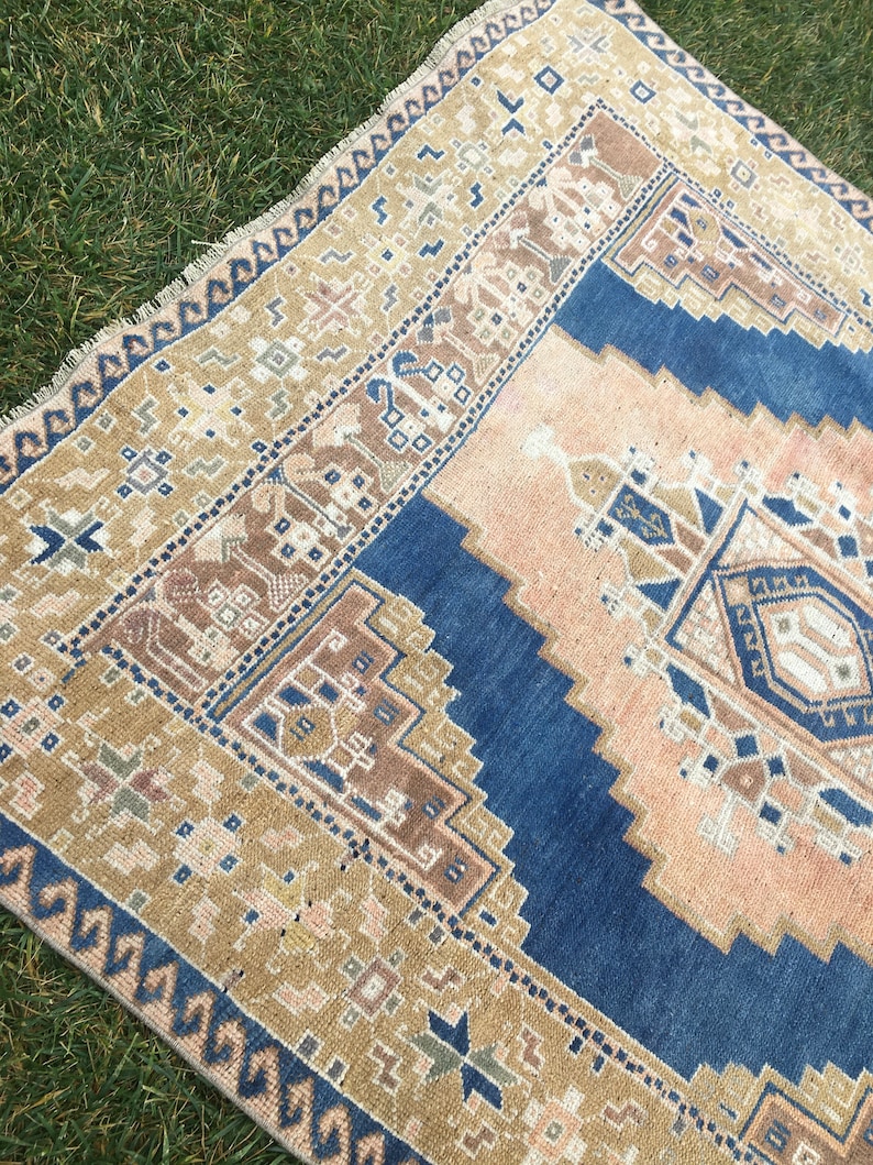 May include: A vintage rug with a blue, beige and brown geometric pattern. The rug has a fringed edge and is made of wool.