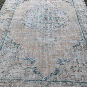May include: A vintage rug with a faded beige background and a teal floral pattern. The rug has a distressed look and is made of wool.