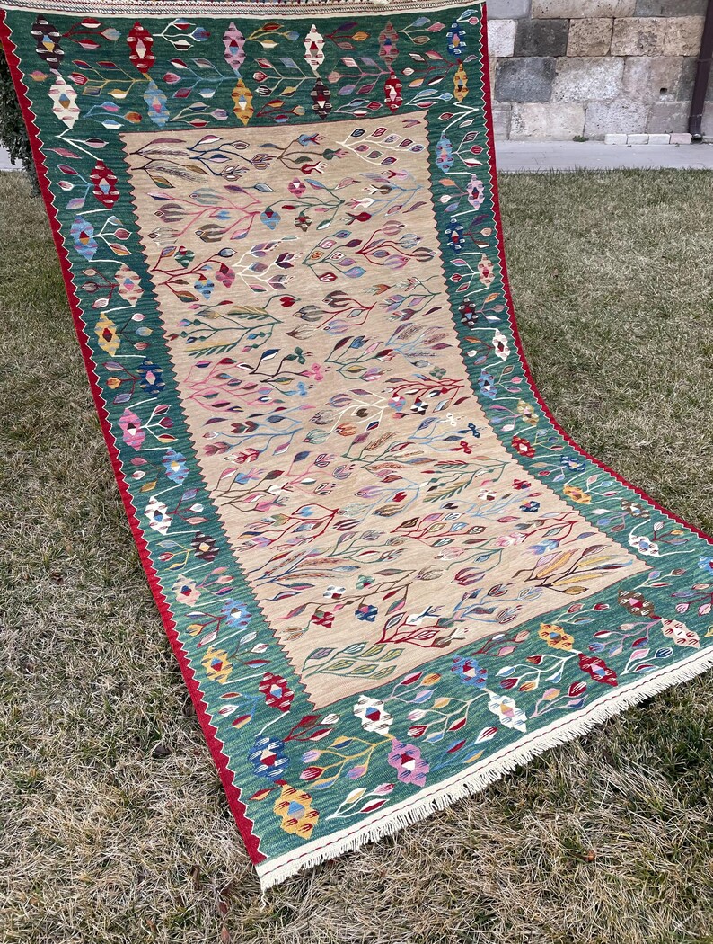May include: A traditional rug with a green, beige and red colour scheme. The rug features a floral pattern with intricate details. The rug is made of wool and has a fringe border.