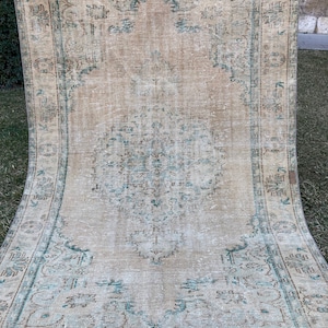 May include: A vintage rug with a faded beige background and a central medallion in shades of teal and brown. The rug has a distressed look with a frayed edge.