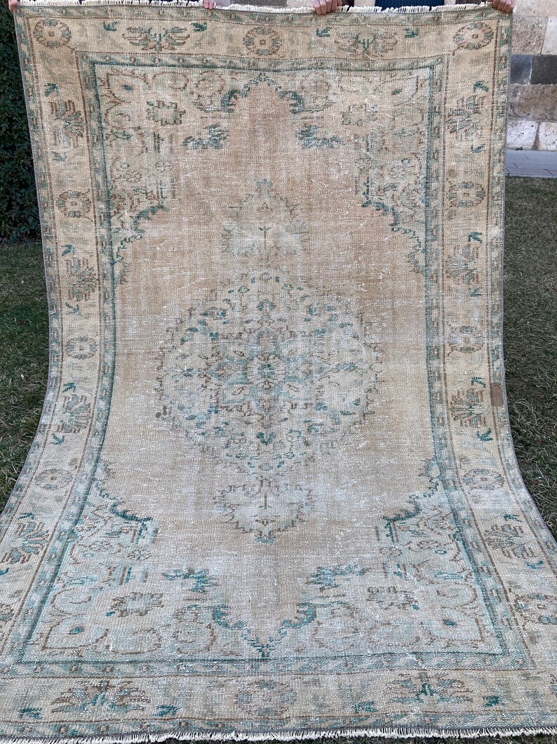 May include: A vintage rug with a faded beige background and a central medallion in shades of teal and brown. The rug has a distressed look with a frayed edge.