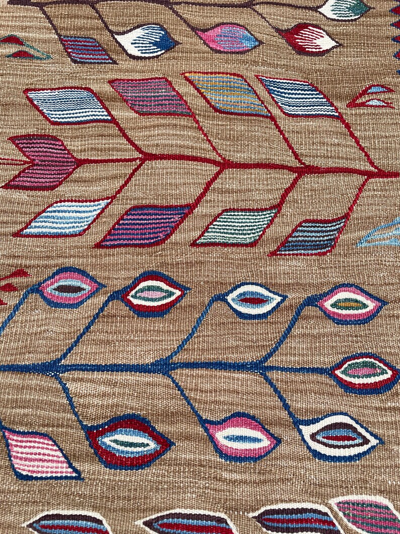 May include: A brown woven rug with a geometric pattern of blue, red, pink, and white leaves and flowers.