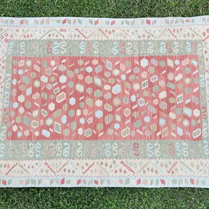 K&ouml;nnte beinhalten: Ein rot-gr&uuml;n-wei&szlig;er Teppich mit Fransenrand. Der Teppich hat ein geometrisches Muster mit verschiedenen Formen und Farben.