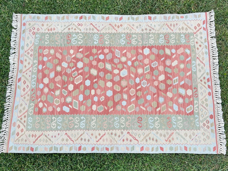 K&ouml;nnte beinhalten: Ein rot-gr&uuml;n-wei&szlig;er Teppich mit Fransenrand. Der Teppich hat ein geometrisches Muster mit verschiedenen Formen und Farben.