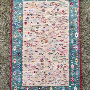 May include: A colourful rug with a green border and a beige centre featuring a floral pattern. The rug has a fringe border.