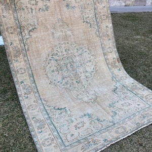 May include: A vintage rug with a light beige background and a teal blue pattern. The rug has a faded look and a fringed edge.