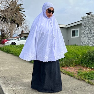 May include: A white prayer shawl with lace trim and a black skirt. The shawl is worn over the head and covers the shoulders and chest. The person wearing the shawl is wearing sunglasses.