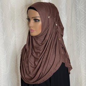 May include: A brown jersey hijab with a gathered design and decorative rhinestone accents.