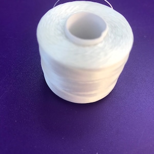 May include: A spool of white thread, tightly wound around a central core. A single strand of thread arches over the top. The spool is set against a purple background.