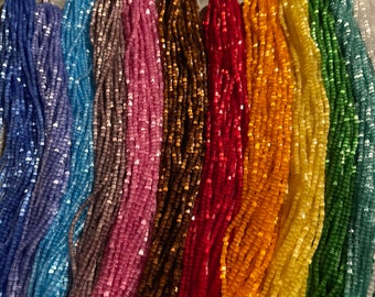 Könnte beinhalten: Sortiment aus 10 Strängen quadratischer Glasperlen in verschiedenen Farben, darunter Blau, Lila, Braun, Rot, Gelb, Grün und Weiß. Die Perlen sind in einer Reihe angeordnet, wobei die Farben von Blau nach Weiß übergehen.