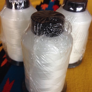 May include: Three spools of white thread wrapped in clear plastic, each with a black plastic cap.