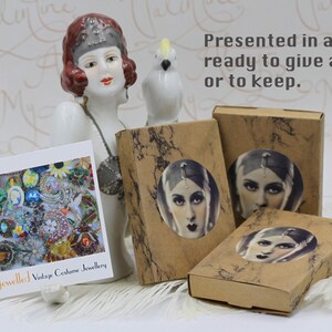 May include: An arrangement of vintage costume jewelry, presented in boxes with a vintage portrait. The boxes are brown with a marble design. A card displays various colorful brooches and jewelry. Text reads "Bejewelled Vintage Costume Jewellery."