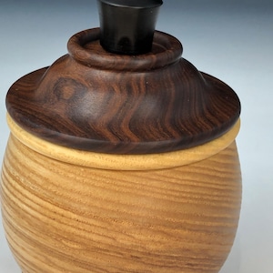 May include: A wooden box with a lid made of dark wood with a black knob on top. The box is made of light wood with a grain pattern.