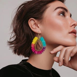 May include: A pair of vibrant, teardrop-shaped earrings. The earrings feature a gold-colored frame and are adorned with colorful, fringed accents in shades of yellow, pink, blue, and purple. The earrings are designed to be worn on the ear.