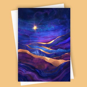May include: Greeting card featuring an abstract landscape with a starry night sky. The design showcases layered blue, purple, and gold tones, with a bright starburst in the center. The card is set against a white envelope.
