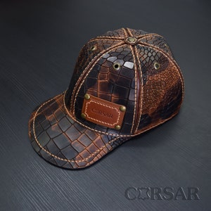 Op de afbeelding: Een bruine leren baseballpet met een krokodilpatroon en een bruin leren patch met de tekst "CERSAR".