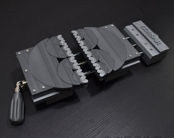 Op de afbeelding: Een zwarte metalen klem met een reeks in elkaar grijpende tandwielen. De klem is open en heeft een handvat aan de zijkant. De tekst "CIRSAR" is gedrukt op de zijkant van de klem.