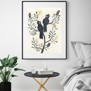 May include: A framed print of three black cockatoos perched on a branch of a stylized tree with yellow flowers. The background is a light cream color.