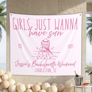 May include: A white banner with pink text that reads "GIRLS, JUST WANNA have sun" and "Jessie's Bachelorette Weekend CHARLESTON, SC". A pink illustration of a person in the water is in the center. The banner is hanging outside.
