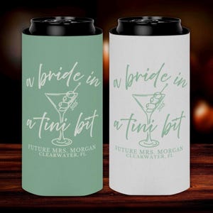 Op de afbeelding: Twee blikjeskoelers, één in mintgroen en één in wit, met zwarte deksels. Elke koeler heeft de tekst "a bride in a tini bit" met een martini-glasafbeelding en "Future Mrs. Morgan Clearwater, FL".