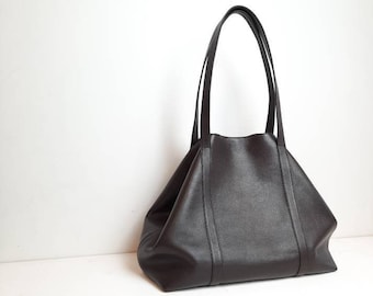 May include: A large, brown leather tote bag with two handles. The bag has a slightly slouchy shape and is made of a textured leather.