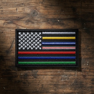 May include: A rectangular embroidered patch featuring a black background with a white star field in the upper left corner. The design includes horizontal stripes in silver, yellow, blue, white, red, blue, and green, all bordered by black stitching.