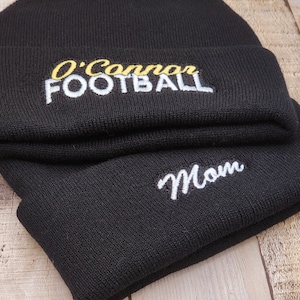 May include: Two black knit beanies with white and yellow embroidery. The top beanie has the text "O'Connor FOOTBALL" and the bottom beanie has the text "Mom".