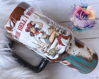 May include: A white and brown tumbler with a glittery finish. The tumbler features a vintage illustration of a woman in a red cowboy hat and blue jeans with the text "The Hell I Won't".