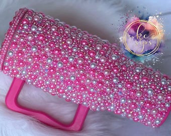 May include: Pink tumbler with a handle, covered in pink and white pearls.