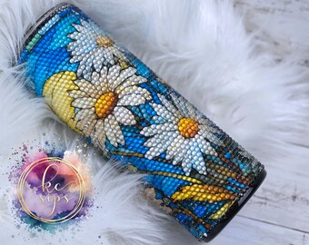 May include: A blue and white tumbler with a daisy design. The tumbler is covered in rhinestones.
