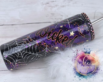 May include: A black and purple glitter tumbler with a spiderweb design, gold stars, and a bat. The tumbler has the word "wicked" written on it in black with a copper outline. The tumbler has a clear lid with a black and silver straw.