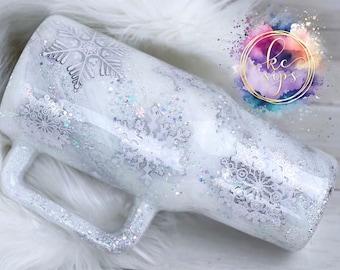May include: White glitter tumbler with a snowflake design. The tumbler has a handle and is perfect for hot or cold beverages.