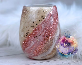 May include: A white and pink tumbler with gold glitter and a marbleized design. The tumbler is made of stainless steel and has a double-walled construction to keep drinks cold or hot for hours.