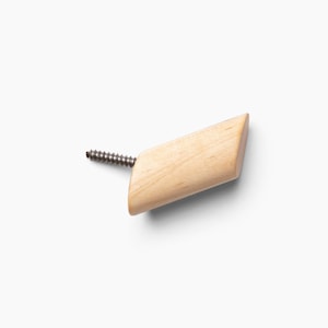 May include: A wooden hook with a screw for attaching to a wall. The hook is light brown and has a slightly angled shape.