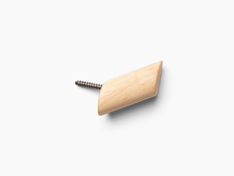 May include: A wooden hook with a screw for attaching to a wall. The hook is light brown and has a slightly angled shape.
