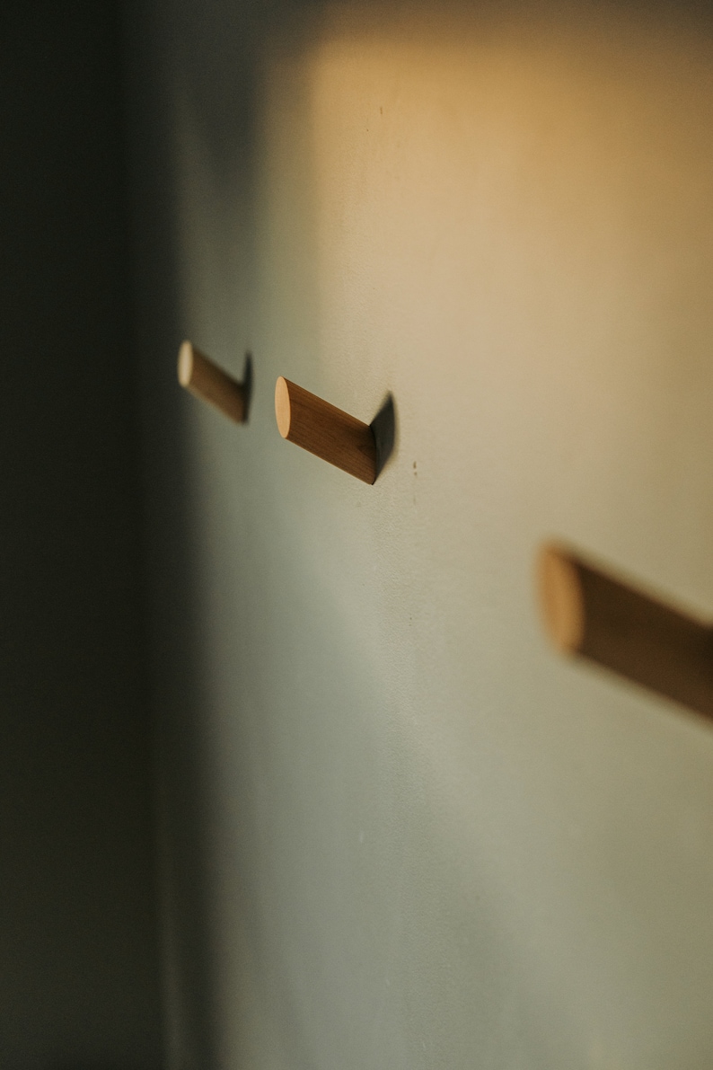 May include: Three wooden wall hooks mounted on a light green wall. The hooks are cylindrical and are arranged in a row.