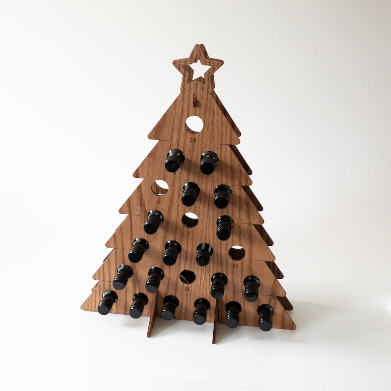 Puede incluir: Porta botellas de madera con forma de &aacute;rbol de Navidad con 24 ranuras numeradas para botellas peque&ntilde;as. El &aacute;rbol est&aacute; hecho de madera marr&oacute;n claro y tiene una estrella en la parte superior.