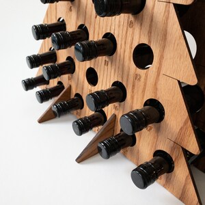 Puede incluir: Porta botellas de vino de madera con forma de &aacute;rbol de Navidad con 12 ranuras. El soporte est&aacute; hecho de madera marr&oacute;n claro y tiene un acabado de veta de madera natural. Las ranuras est&aacute;n numeradas del 1 al 12. El soporte est&aacute; sobre una superficie blanca.